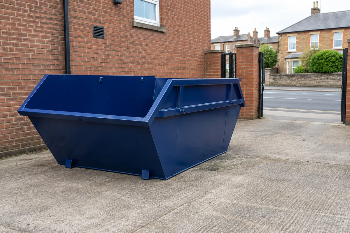 Empty blue skip in a private paved yard beside a brick building